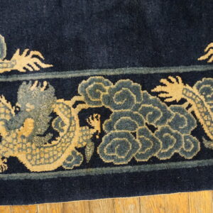 Close-up of a high-pile navy rug border with tan dragons and slate blue cloud motifs on wood plank flooring.