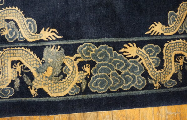Close-up of a high-pile navy rug border with tan dragons and slate blue cloud motifs on wood plank flooring.