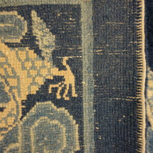 Detail shot of a dense rug showing navy, light blue, and tan geometric patterns and a stylized figure.