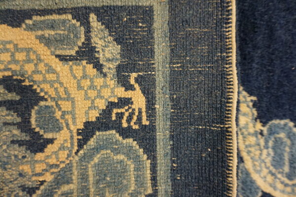 Detail shot of a dense rug showing navy, light blue, and tan geometric patterns and a stylized figure.
