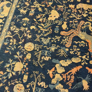 Detailed dark blue rug featuring golden yellow, teal, and orange mythical and floral motifs, with a patterned border on wood floor.