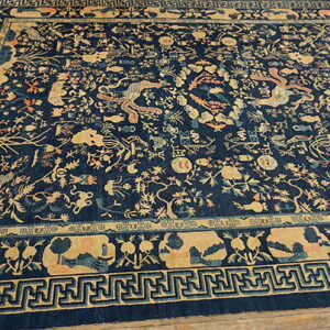 Navy blue rug with a detailed gold and coral Oriental pattern, geometric borders, shown on wood flooring.