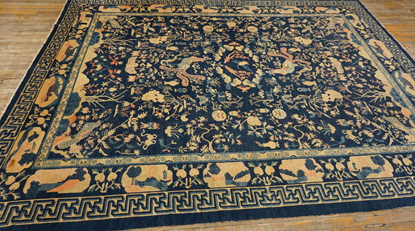 Navy blue rug with a detailed gold and coral oriental pattern, geometric borders, shown on wood flooring.