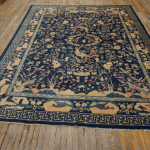 A detailed dark blue rug with tan, peach, and light blue traditional patterns rests on a wooden floor.