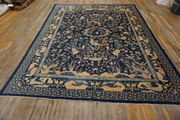 A detailed dark blue rug with tan, peach, and light blue traditional patterns rests on a wooden floor.