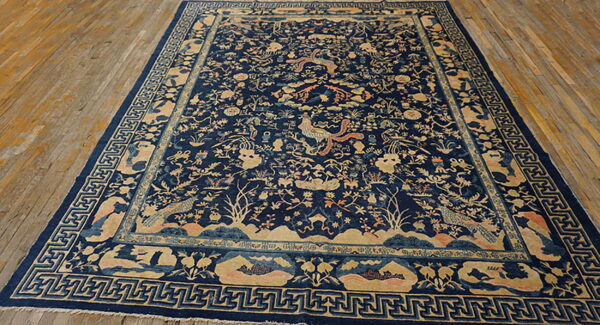 Large dark blue rug with intricate tan and peach traditional patterns on natural wood flooring.