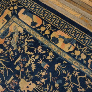 A navy rug with detailed gold and peach floral motifs and geometric key borders rests on distressed wood.
