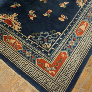 Dark blue rug corner with multi-colored floral and geometric borders rests on distressed wood plank flooring.