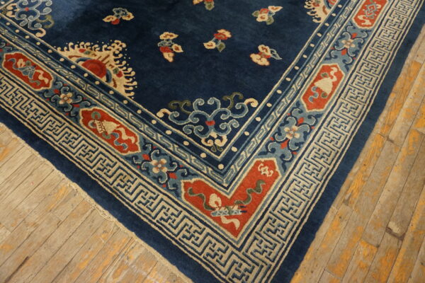 Dark blue rug corner with multi-colored floral and geometric borders rests on distressed wood plank flooring.