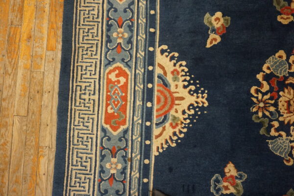 Navy rug with elaborate terracotta, light blue, and cream borders resting on distressed wooden planks.