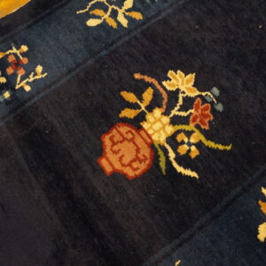 Dark blue high-pile rug with colorful stylized floral vase motif on hardwood floor.