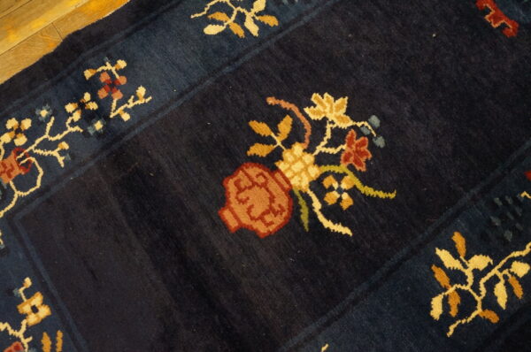 Dark blue high-pile rug with colorful stylized floral vase motif on hardwood floor.