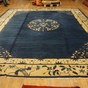 Large navy blue and gold rug featuring a central medallion and wide floral borders on a wooden floor.
