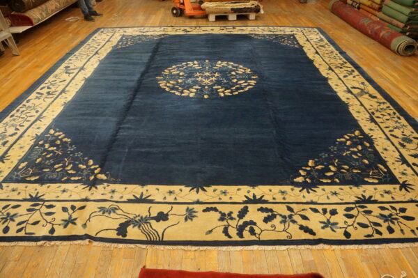 Large navy blue and gold rug featuring a central medallion and wide floral borders on a wooden floor.