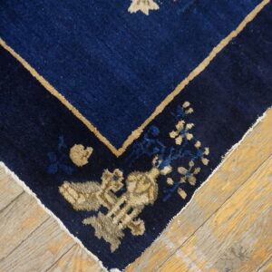 Dark blue area rug with tan and light blue floral designs shown on wide, textured wood planks.