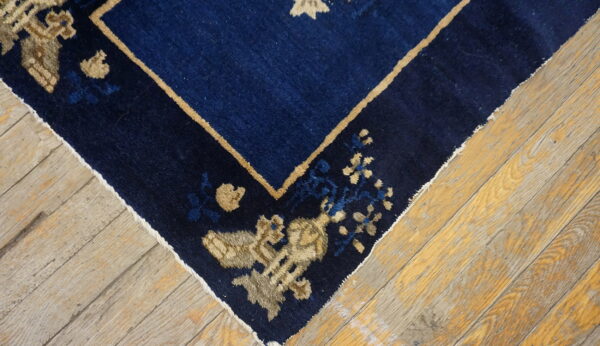 Dark blue area rug with tan and light blue floral designs shown on wide, textured wood planks.