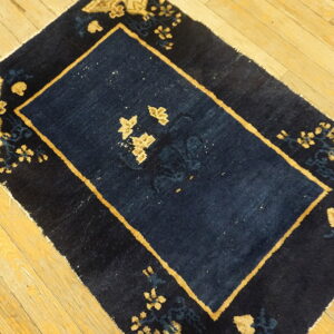 Navy blue rug featuring tan borders and floral designs rests on a rustic light wood plank floor.