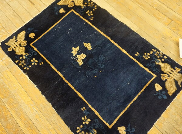 Navy blue rug featuring tan borders and floral designs rests on a rustic light wood plank floor.