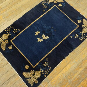 Small dark blue rug with a central panel and tan patterned border rests on plank wood flooring.