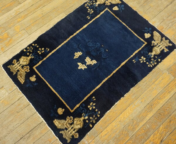 Small dark blue rug with a central panel and tan patterned border rests on plank wood flooring.