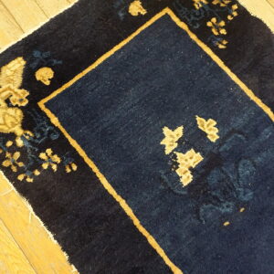 Navy blue area rug with medium pile and gold botanical pattern shown on hardwood floor.