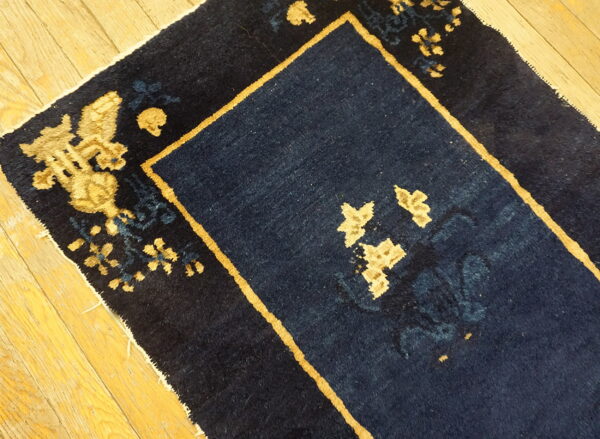 Navy blue area rug with medium pile and gold botanical pattern shown on hardwood floor.