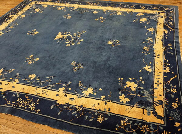 Rectangular blue rug featuring scattered yellow botanical designs and a wide, golden border on wood planks.