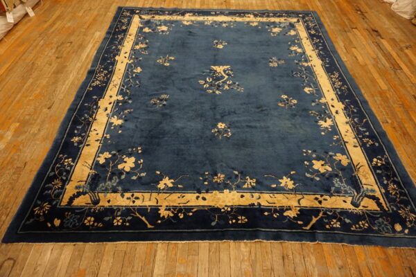 Deep blue rug with gold floral borders and scattered motifs displayed on rustic hardwood flooring.