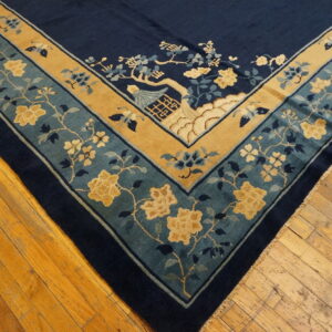 Corner of a blue rug shows teal and gold borders with yellow floral and scenic patterns on wood planks.