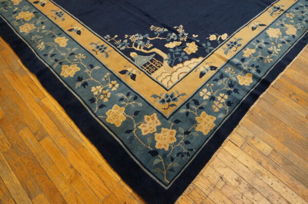 Corner of a blue rug shows teal and gold borders with yellow floral and scenic patterns on wood planks.