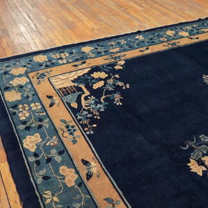 Navy blue rug with tan and teal borders featuring florals rests on distressed wood planks.