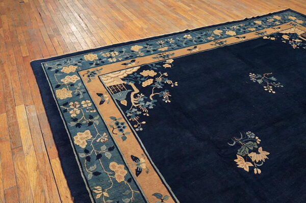 Navy blue rug with tan and teal borders featuring florals rests on distressed wood planks.