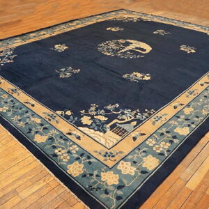 Navy blue area rug with scattered ivory and teal floral patterns, bordered in tan on wood flooring.