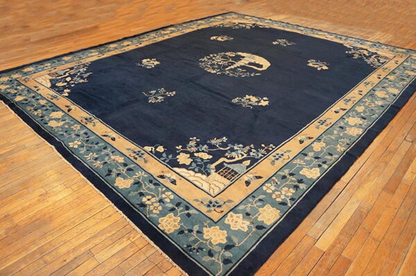 Navy blue area rug with scattered ivory and teal floral patterns, bordered in tan on wood flooring.