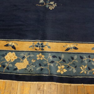 Navy rug with detailed gold and teal floral borders rests on honey-toned wooden plank flooring.