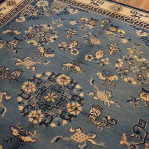 Low-pile blue rug with contrasting tan and navy stylized medallions and a geometric fretwork border.