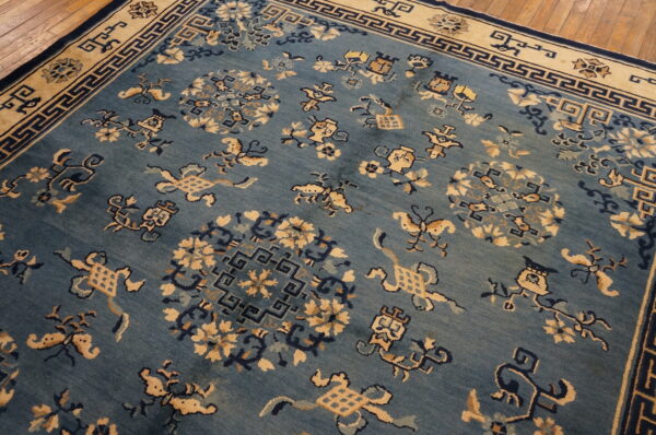Low-pile blue rug with contrasting tan and navy stylized medallions and a geometric fretwork border.