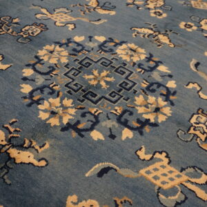 Angled view of a blue rug with a complex traditional pattern of beige, navy, and aqua motifs.