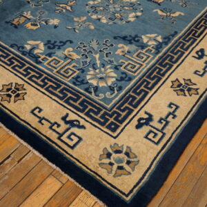 Blue and tan low-pile rug with geometric and floral patterns sits on rustic, wide-plank wood flooring.