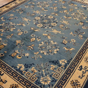 Traditional blue rug with beige and navy geometric border and scattered floral patterns on wood flooring.