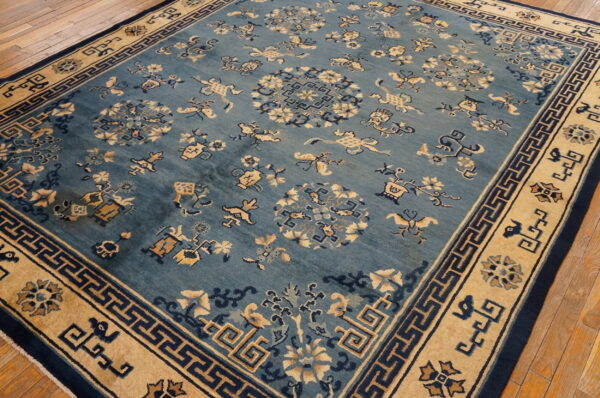 Traditional blue rug with beige and navy geometric border and scattered floral patterns on wood flooring.