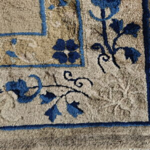 Close-up of a high-pile rug corner with blue floral patterns and borders on a beige field.