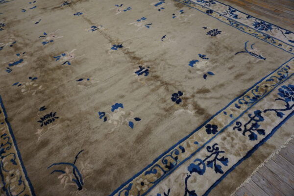 Taupe area rug with scattered blue and cream floral motifs and a detailed blue border on wood floor.
