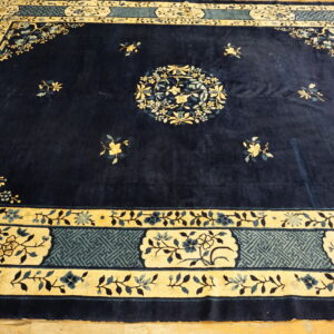 Navy blue rug featuring a central floral medallion and ornate borders in cream and dusty blue on wood flooring.