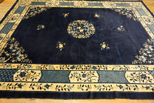Navy blue rug featuring a central floral medallion and ornate borders in cream and dusty blue on wood flooring.