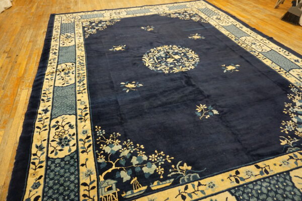 Dark blue rug with contrasting yellow and light blue floral border lies on light wooden floorboards.