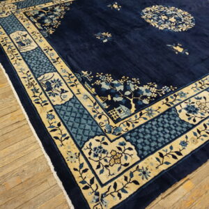 Dark blue rug with gold and light blue floral and geometric borders over distressed wood planks.