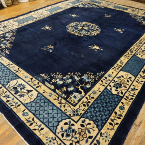 Plush navy rug featuring a traditional cream and blue ornate border rests on wide plank wood flooring.