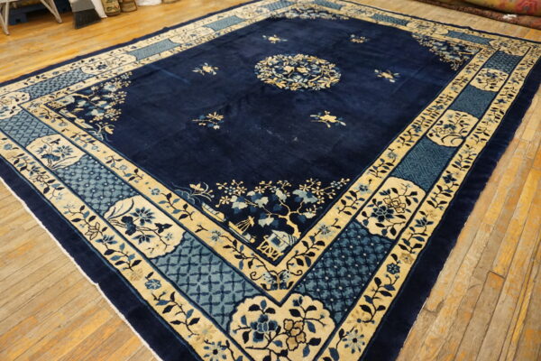 Plush navy rug featuring a traditional cream and blue ornate border rests on wide plank wood flooring.