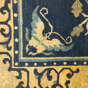 Deep blue rug corner with golden yellow and aqua botanical patterns on a visible medium pile.